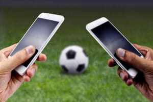 dos personas apostando con sus smartphones en cada mano cancha de fútbol pelota de fútbol